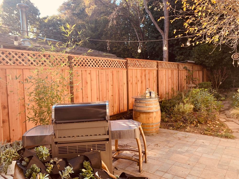 Grill and outdoor seating in a serene backyard with wooden fence and greenery.