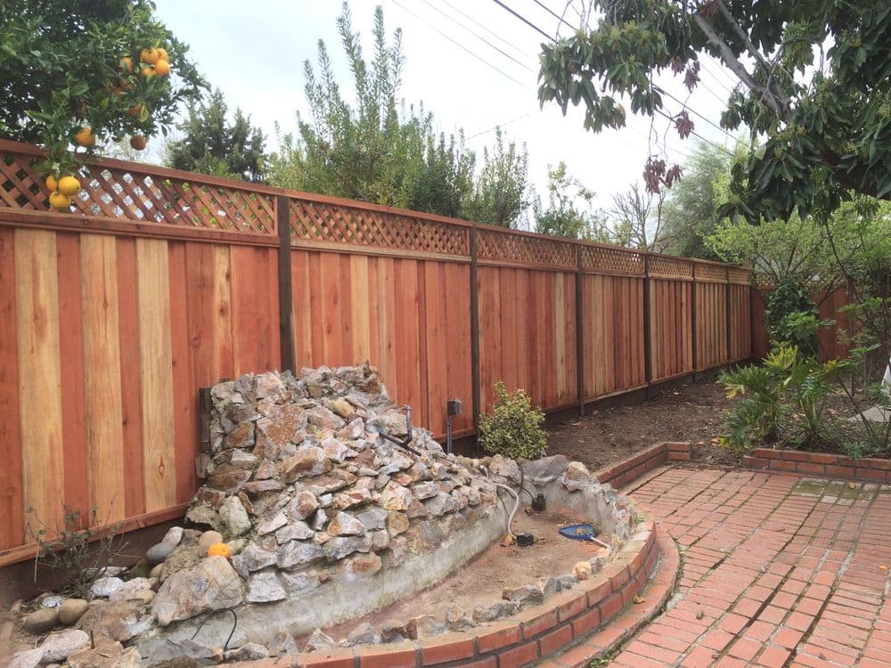 Wooden fence with lattice top and stone feature in a landscaped garden.