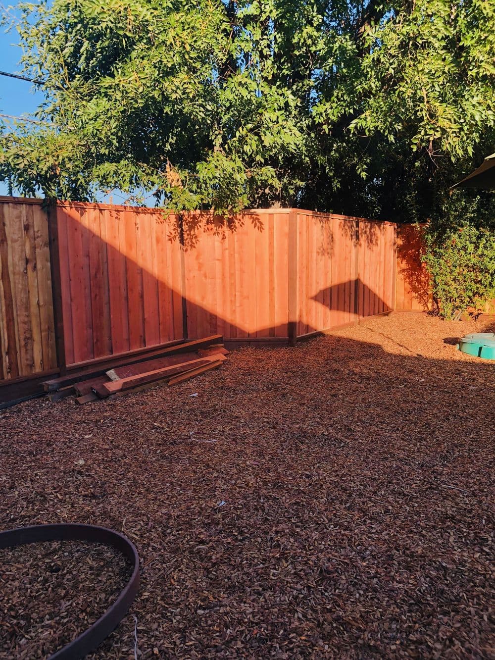 Wooden fence casting a shadow on a gravel-covered yard under a clear blue sky.