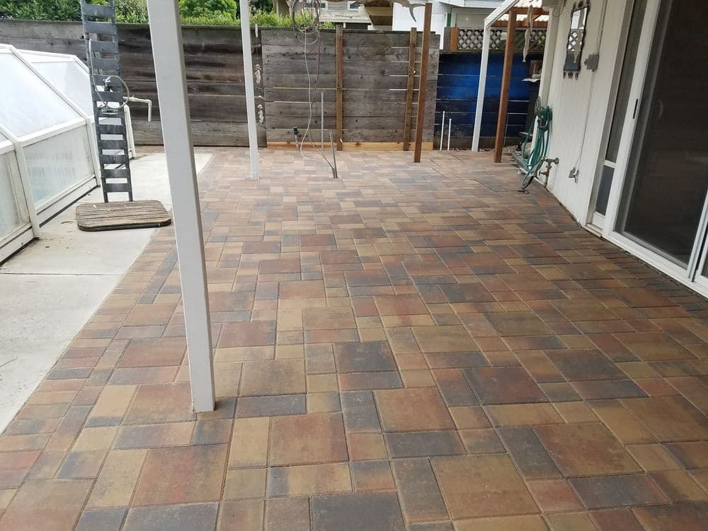 Paved outdoor patio area with textured bricks and a wooden fence in the background.