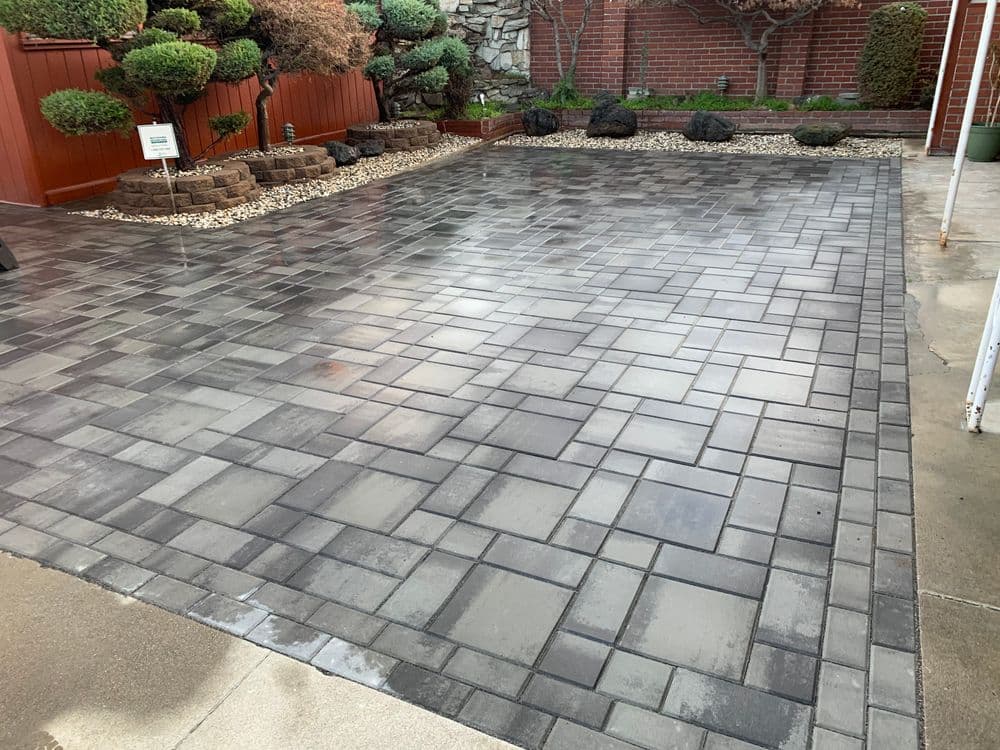 Patterned gray paving stone patio with landscaped garden features and decorative rocks.