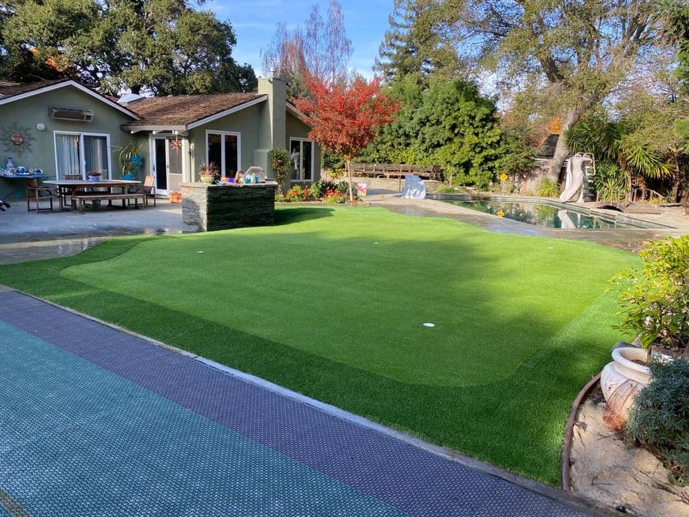 Lush green backyard with artificial turf, pool, and scenic landscaping.