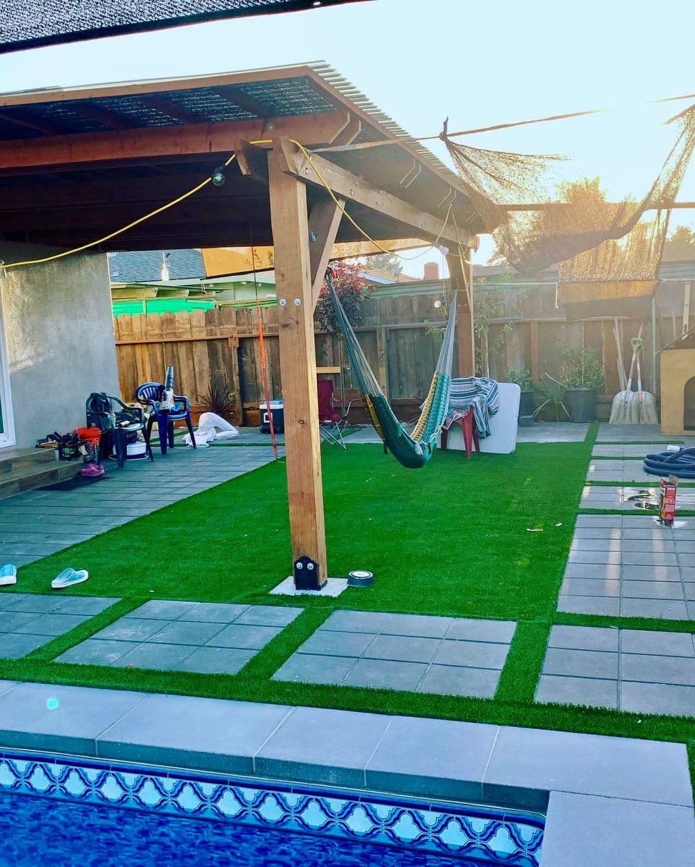 Backyard with synthetic grass, hammock, patio furniture, and a pool under sunset lighting.