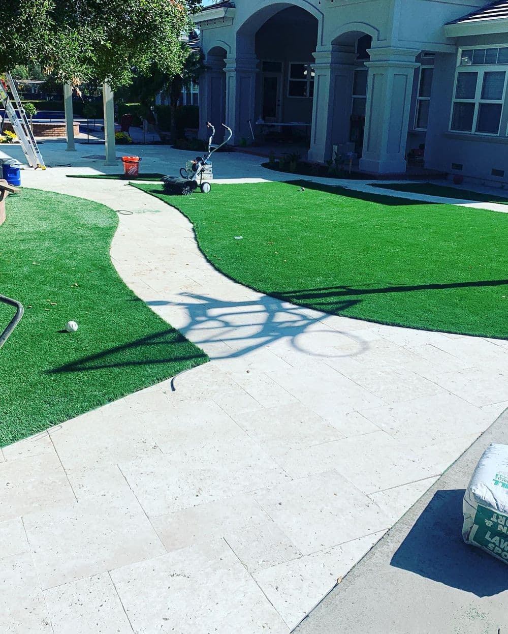 Artificial turf installation in a landscaped yard with a stone pathway and shadowed bicycle.