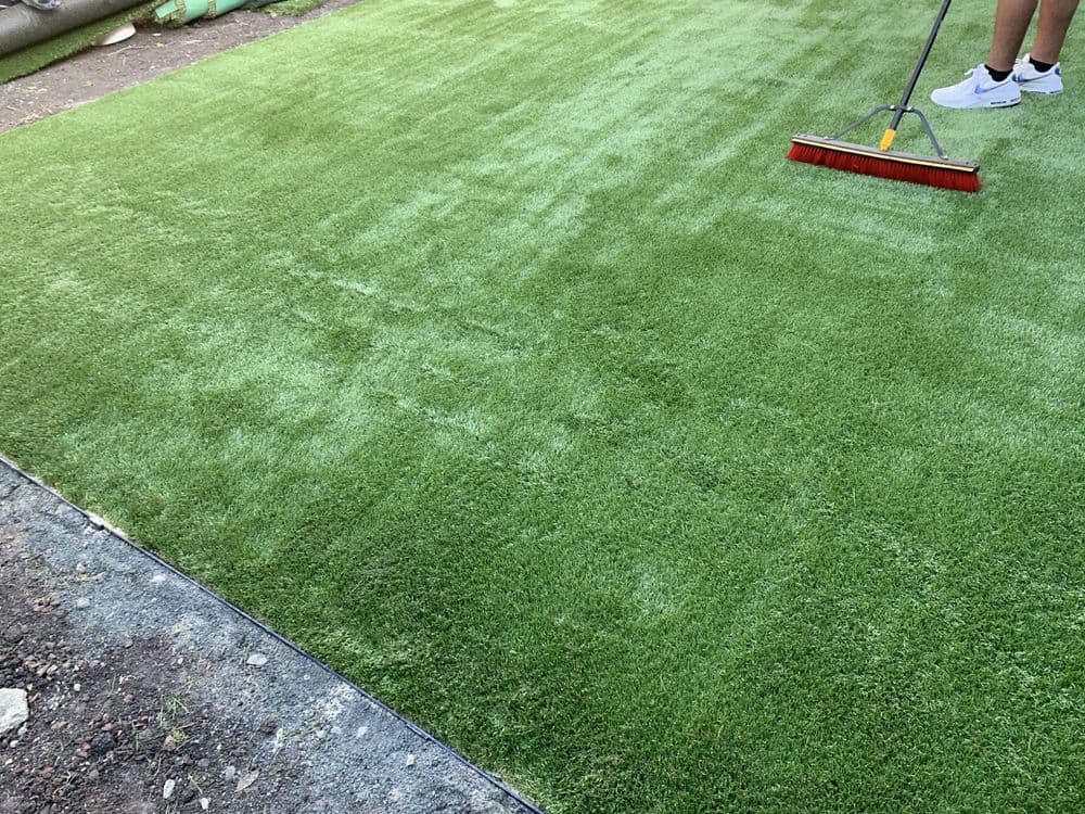 Laying artificial grass with a broom on a freshly prepared lawn surface.