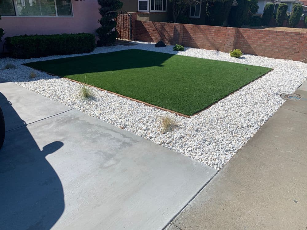 Artificial turf lawn surrounded by white gravel and low shrubs in a residential yard.