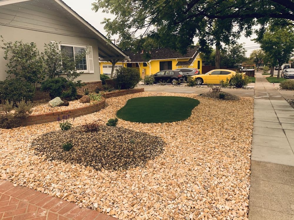 Modern landscape design featuring a rock garden with greenery and a bordered lawn in a residential area.