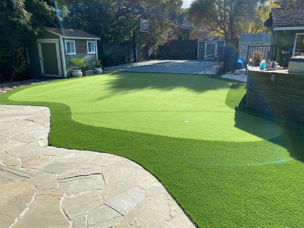 Artificial turf lawn with landscaped stone patio and nearby basketball court in a backyard.